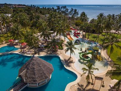Eine tropische Hotelanlage mit Pool, Palmen und Kinderspielplatz am Meer.