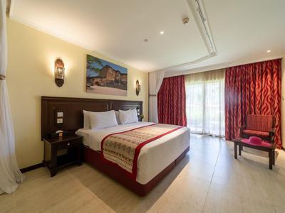 Modernes Hotelzimmer mit großem Bett, Nachttischen, roten Vorhängen und Zugang zu Balkon oder Terrasse.