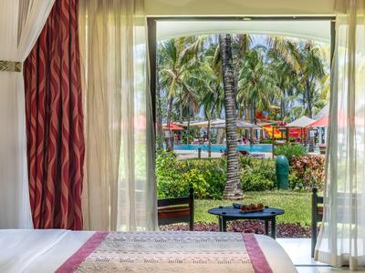 Blick durch ein Vorhangfenster auf tropischen Garten mit Pool und Palmen von Hotelzimmer.