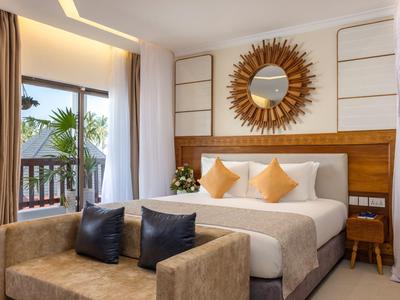 Helle Hotelzimmer mit großem Bett, Sonnenspiegel, Sofa und Balkon mit Pflanzen.