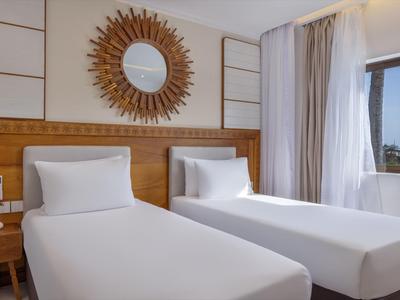 Helles Hotelzimmer mit zwei Einzelbetten, Holzwänden und rundem Dekospiegel über dem Bett.