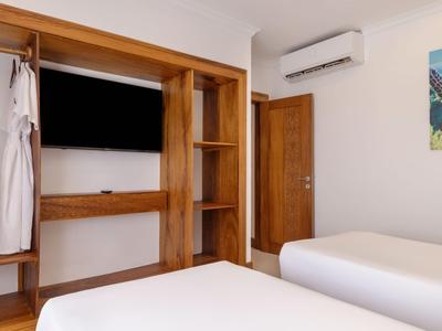 Modernes Hotelzimmer mit zwei Betten, Holzschrank und Klimaanlage an weißer Wand.