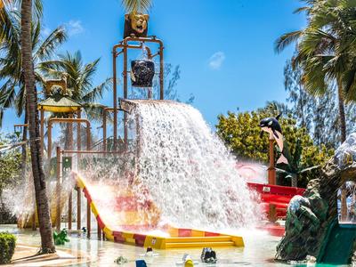 Wasserfall aus Wasserrutsche in tropischem Hotelwasserpark mit Palmen und strahlend blauem Himmel.