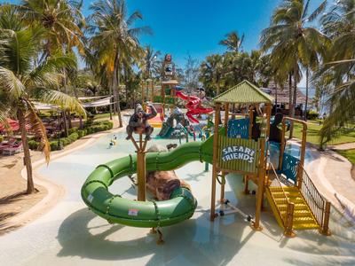Kinder spielen auf einem bunten Spielplatz mit Wasserrutschen umgeben von Palmen.