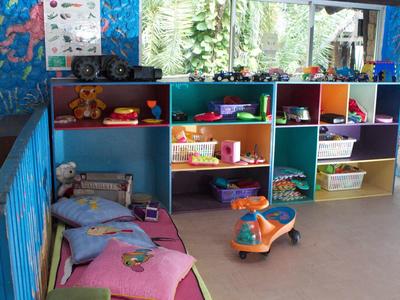 Barevná herní zóna s policemi, hračkami a polštáři u okna.