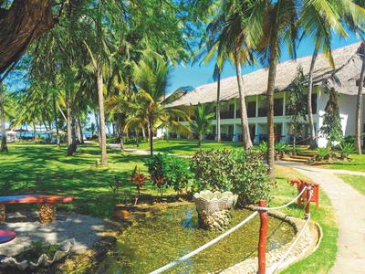 Grüner Hotelgarten mit Palmen, Wegen und Bänken unter strahlend blauem Himmel.