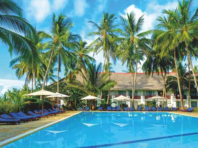 Blauer Pool mit Liegestühlen, Sonnenschirmen und hohen Palmen unter blauem Himmel.