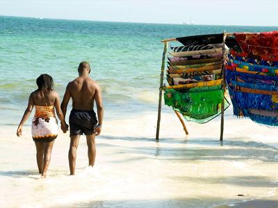Ein Paar geht am Strand ins Wasser, neben einem Stand mit bunten Tüchern.