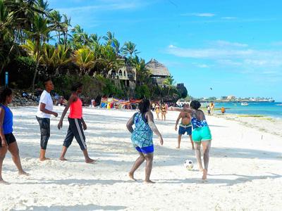 Menschen laufen und spielen am sonnigen Strand mit Palmen.