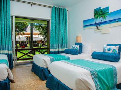 Světelný hotelový pokoj se dvěma jednolůžky, tyrkysovými přikrývkami a výhledem na zahradu.