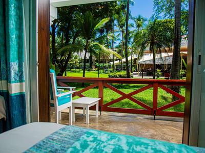 Výhled z hotelového pokoje s terasou na slunnou zahradu s palmami.