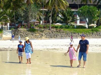 Pláž s lidmi chodícími blízko vody a tropickými rostlinami v pozadí.