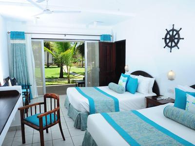 Světle zařízený hotelový pokoj se dvěma postelemi, modrobílým povlečením a výhledem na zahradu s palmami.