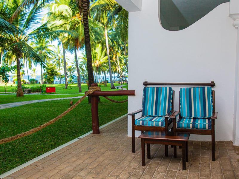 Dva modré židle a malý stolek na terase s výhledem na tropickou zahradu.