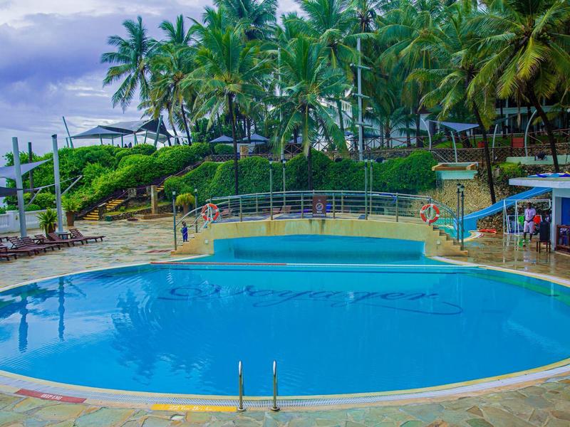 Kruhový hotelový bazén s palmami a lehátky za oblačného dne.