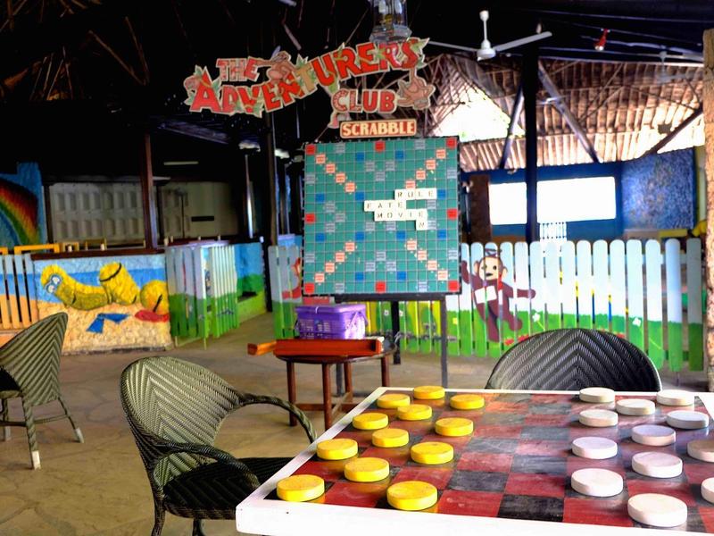 Barevná krytá herní plocha s velkou hrací deskou a ratanovým nábytkem v tropickém prostředí.