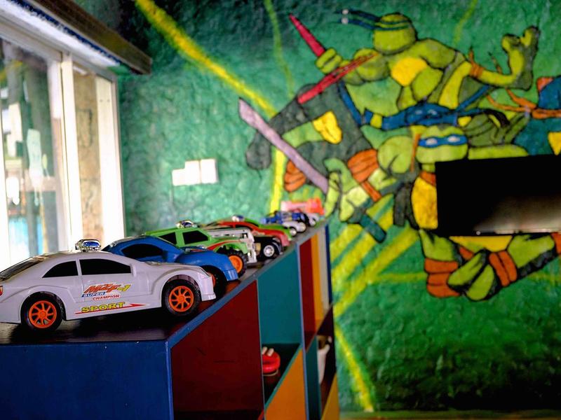 Barevná stěna dětského pokoje s malbou Teenage Mutant Ninja Turtles a hračkami aut na policích.