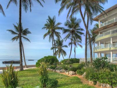 Mehrstöckiges Hotel neben einem grünen Garten mit Palmen, Blick auf das Meer und blauen Himmel.