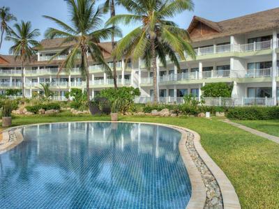 Moderner Hotelkomplex mit riesigem Pool, grüner Wiese und hohen Palmen bei klarem Himmel.