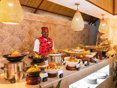 Buffet mit vielfältigen Speisen und einem Koch in roter Weste, warme Beleuchtung, gemütliche Atmosphäre.