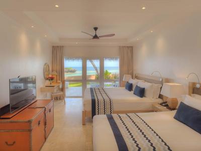 Helles Hotelzimmer mit zwei Queensize-Betten, Fernseher, Ventilator und Meerblick durch große Fenster.