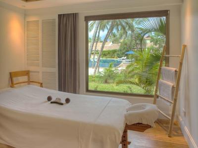 Hell eingerichteter Wellnessraum mit Massageliege, großem Fenster und pflanzlicher Aussicht.