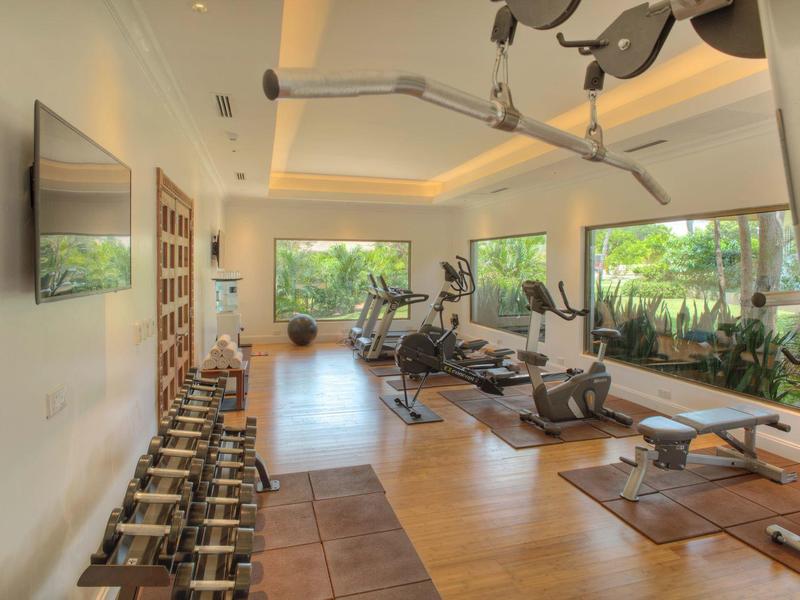 Moderner Fitnessraum mit Hanteln, Geräten, großen Fenstern und Blick auf grünen Garten.