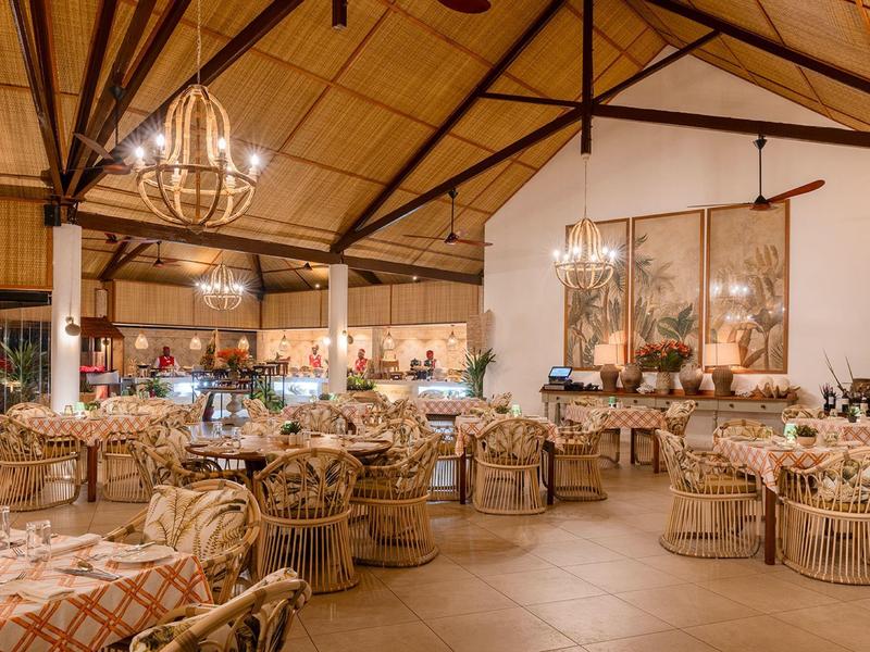 Großer, rustikaler Speisesaal mit Holzstühlen, Kronleuchtern und Deckenbalken in warmem Licht.