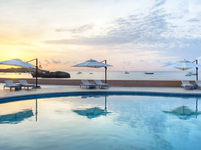 Ruhiger Pool mit Sonnenschirmen und Liegen am Meer bei Sonnenuntergang.