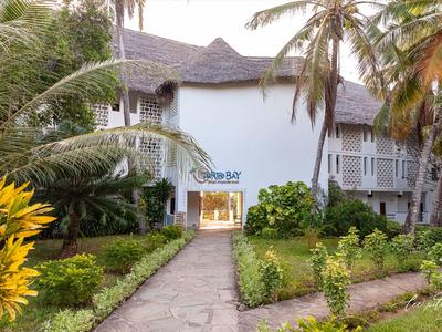Ingresso di un hotel con edificio bianco, palme e sentiero del giardino curato.