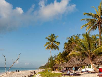 Spiaggia con palme, sedie a sdraio e capanne di paglia sotto un cielo blu con nuvole