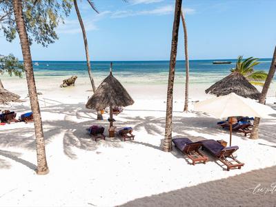 Spiaggia di sabbia bianca con lettini e ombrelloni di paglia circondata da palme e mare blu.