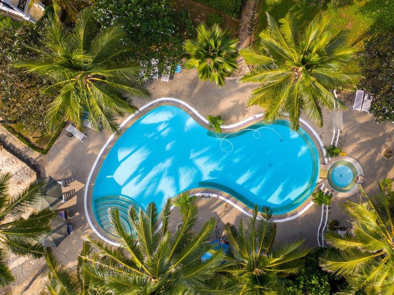 Buitenzwembad in een tropisch hotel, omgeven door palmbomen en parasols.