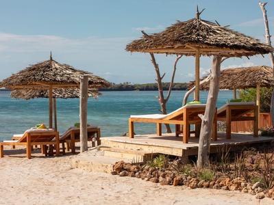 Strand mit Holzliegen und Strohsonnenschirmen am klaren blauen Meer unter blauem Himmel.