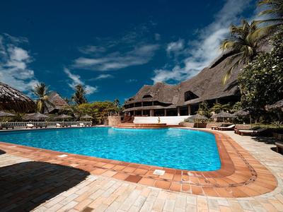 Freizeitpool mit klar blauem Wasser vor einem Hotel unter blauem Himmel mit Palmen.