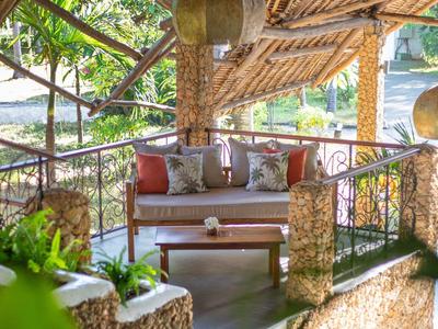 Gemütliche Lounge Ecke mit Sofa und Kissen unter einem offenen Dach aus Naturmaterialien.