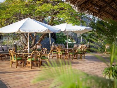 Außenbereich eines Hotels mit Holzstühlen und Tischen unter weißen Sonnenschirmen auf einer Terrasse.