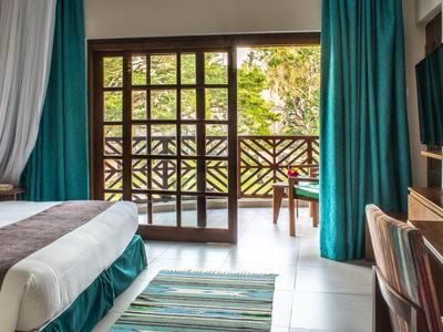 Modernes Hotelzimmer mit Doppelbett, Teppich und großem Fenster mit Blick auf Balkon und Garten