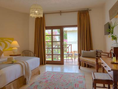 Chambre d'hôtel confortable avec deux lits simples, coin salon et accès balcon avec vue sur le jardin.