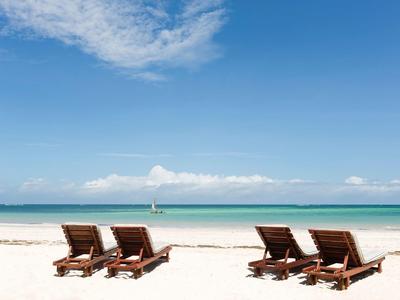 Quatre chaises longues en bois sur une plage de sable blanc face à la mer turquoise calme et au ciel bleu.