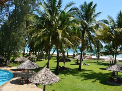 Jardin tropical vert avec des palmiers et parasols en chaume près d'une piscine avec vue sur la mer.