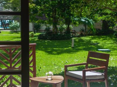 Balcon avec chaise et petite table donnant sur jardin vert sous un temps ensoleillé.