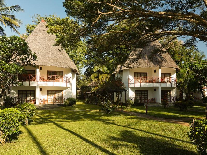 Deux cottages de vacances au toit de chaume entourés d'un jardin vert avec des arbres.