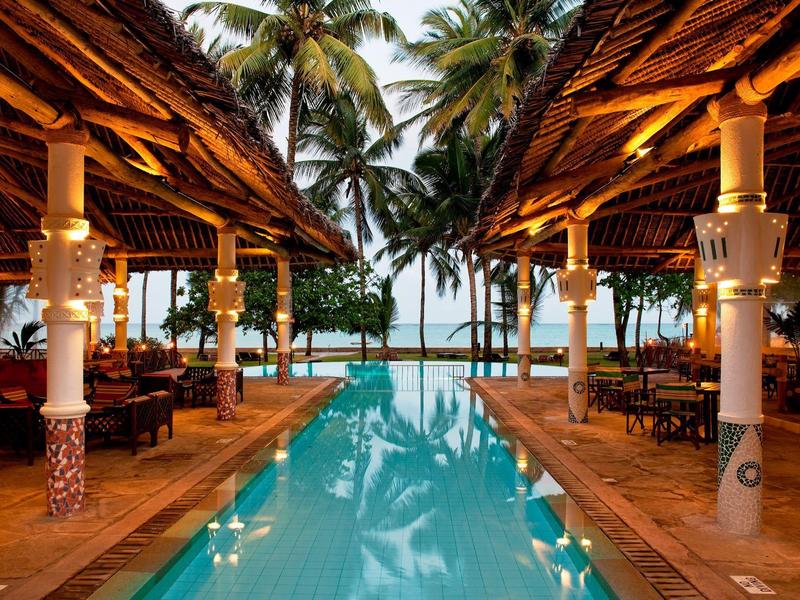 Piscine éclairée dans un complexe tropical avec des palmiers le soir.