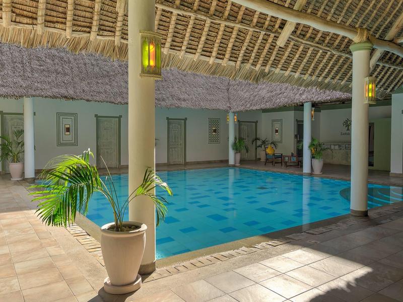 Piscine intérieure couverte avec colonnes et plantes dans une zone d'hôtel.