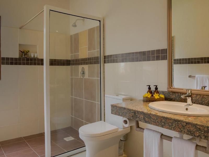 Salle de bain propre avec douche, toilettes, lavabo et grand miroir dans des tons beiges chauds.