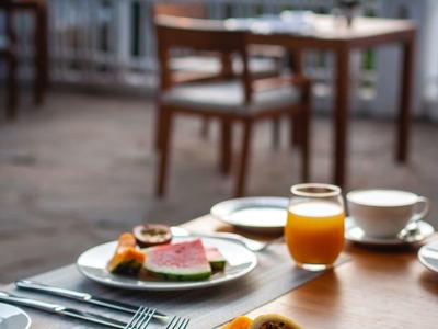 Breakfast table with fresh fruit, juice, and coffee on a terrace with chairs and outdoor view.