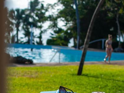Small white table with two cups, sunglasses, and book, view of pool and palm trees.