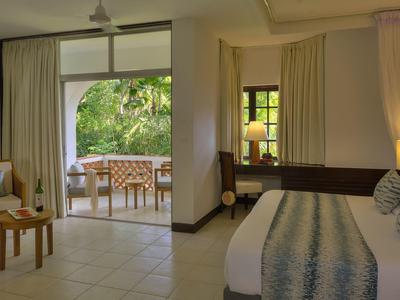 Bright hotel room with bed, chair, and view of a terrace with table and chairs.