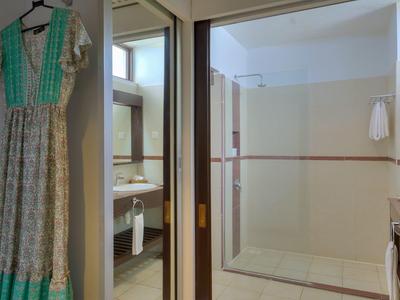 A bright bathroom with shower and mirror, next to it a dress hanging on the wall.